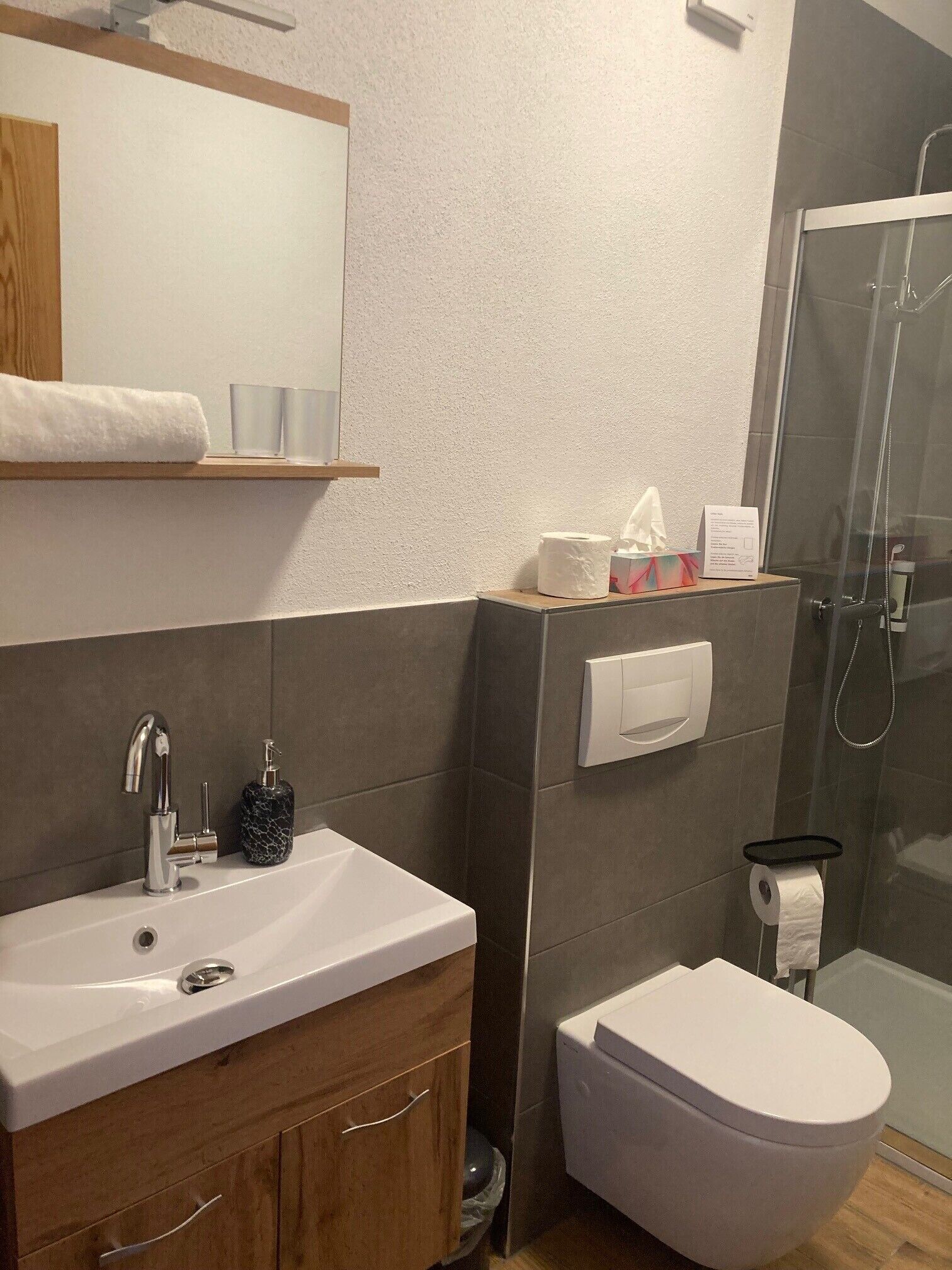 A modern bathroom with a white sink, a mirror, a toilet, and a shower.