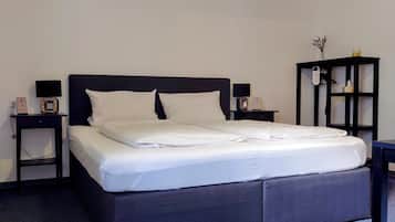 A neatly made bed with white linens, a dark headboard, and a small bedside table with a lamp and a clock.