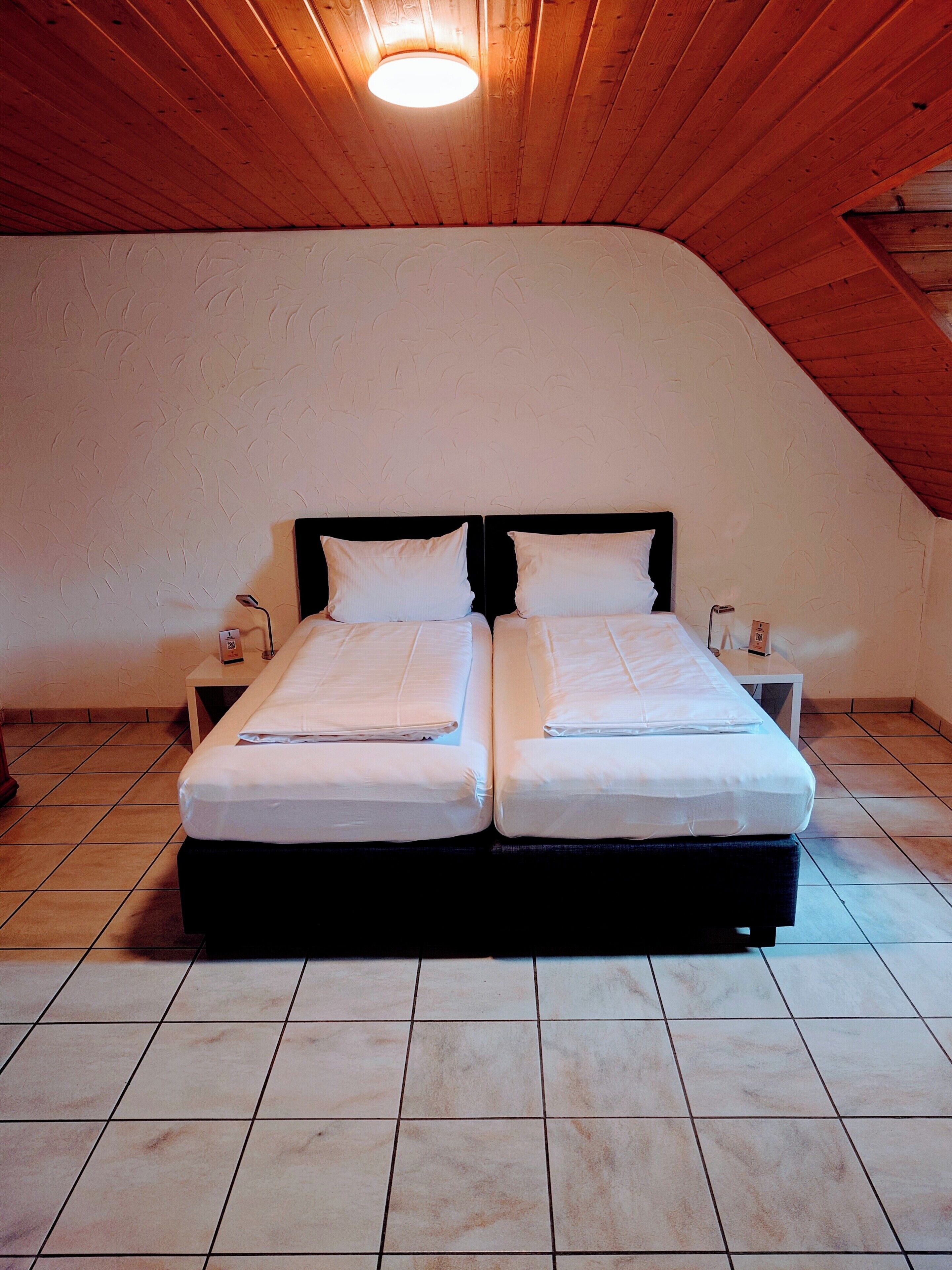 A double bed in a room with a sloped ceiling and tiled floor.