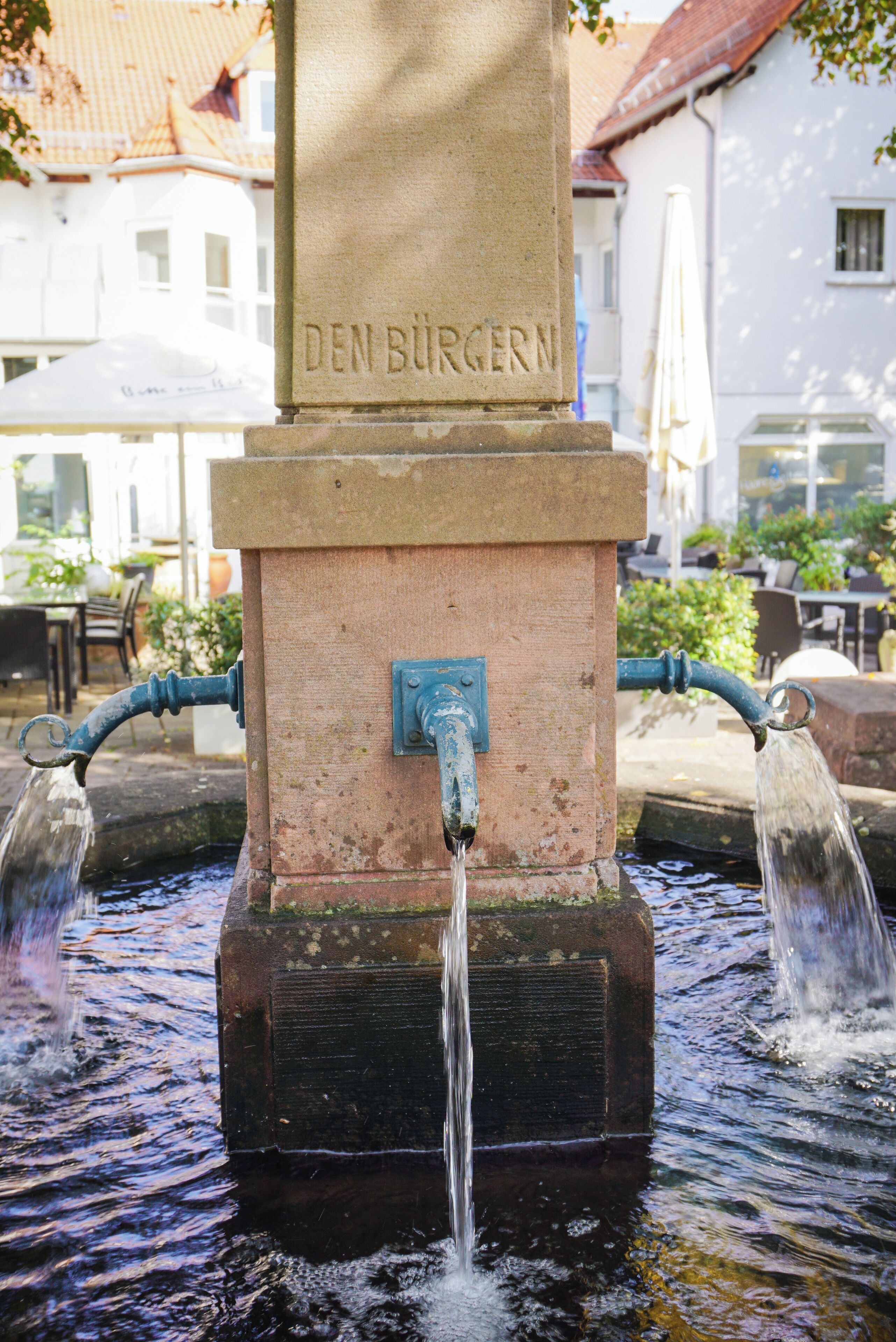 A water pump with the inscription "DEN BURGERN" in a public outdoor setting.