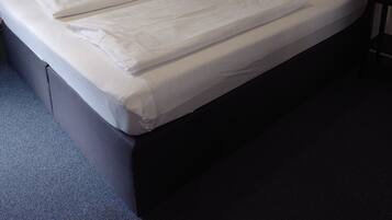 A neatly made bed with white linens, a black headboard, and a nightstand with a lamp and a small item on it.