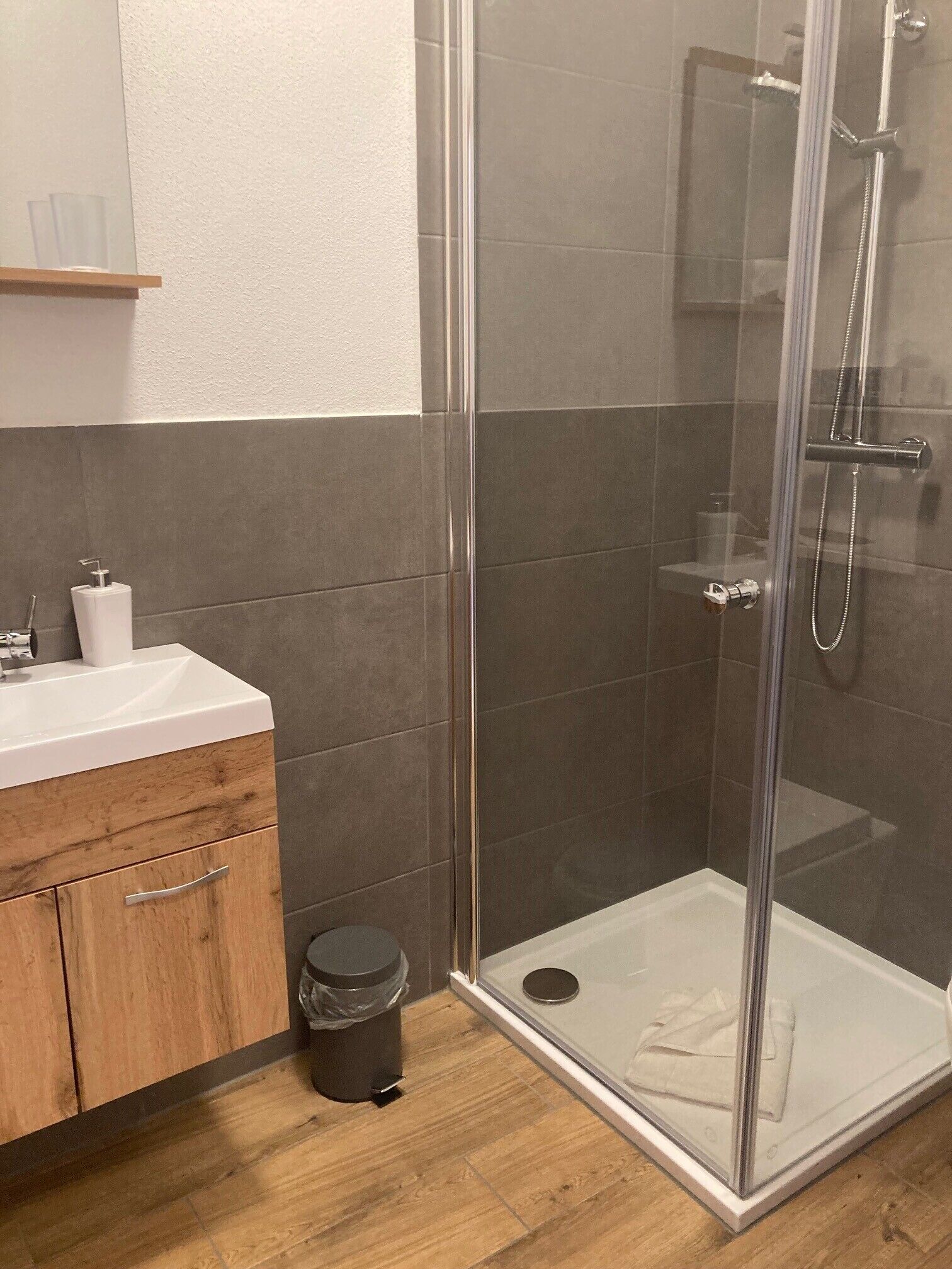 Ein modernes Badezimmer mit einer Duschkabine aus Glas, einem Holzwaschtisch und einem Mülleimer.