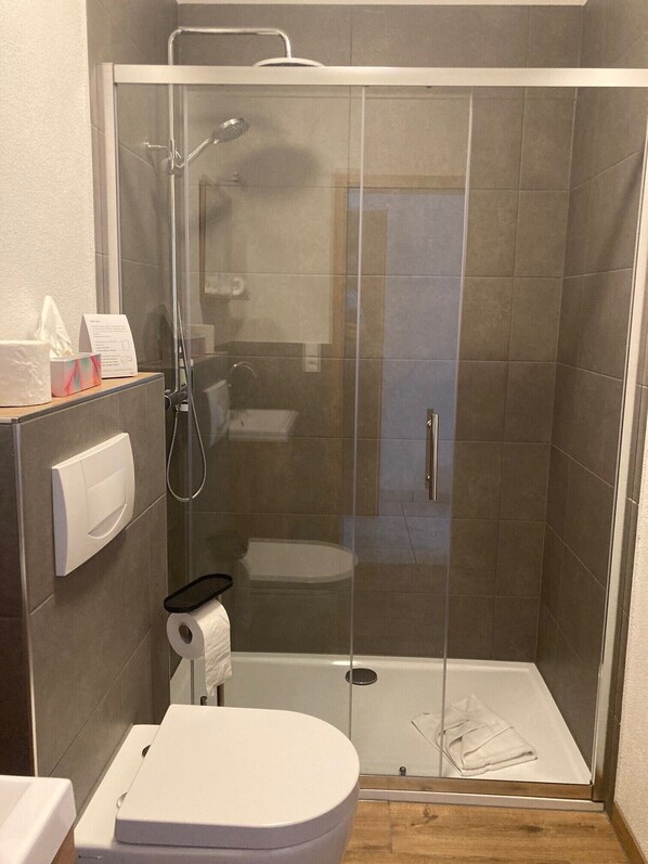 Un baño moderno con ducha envuelta en vidrio, inodoro y secamanos.