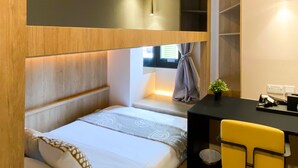 A compact room with a bed, a small desk, and a chair. There is a window with curtains, a plant on the desk, and a shelf with items. - ST Signature Tanjong Pagar, SHORT OVERNIGHT, 12 hours: 8PM-8AM (Singapore)