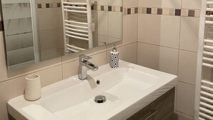 A modern bathroom with a white sink, a mirror, a towel rack, and a soap dispenser. - Beautiful apartment in the center of Folelli (Penta-di-Casinca)