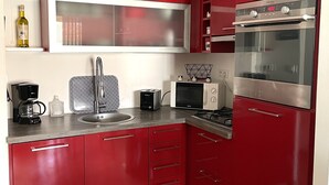 A modern kitchen with red cabinetry, a built-in oven, and a microwave. - Beautiful apartment in the center of Folelli (Penta-di-Casinca)