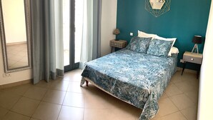 A bedroom with a bed, a nightstand, a lamp, a geometric wall decoration, and a window with curtains. - Beautiful apartment in the center of Folelli (Penta-di-Casinca)