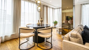 A modern living room with a round dining table, two chairs, a sofa, and a kitchen area in the background. - Apartment 107 - A premium stay that sleeps 4 guests  in 2 bedrooms (York)