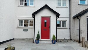 Un bâtiment blanc avec une porte rouge, de nombreuses fenêtres et une enseigne indiquant « Swallows Nest Cottage ».