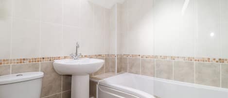 A bathroom with a skylight, white tiles, a sink, toilet, and a bathtub.