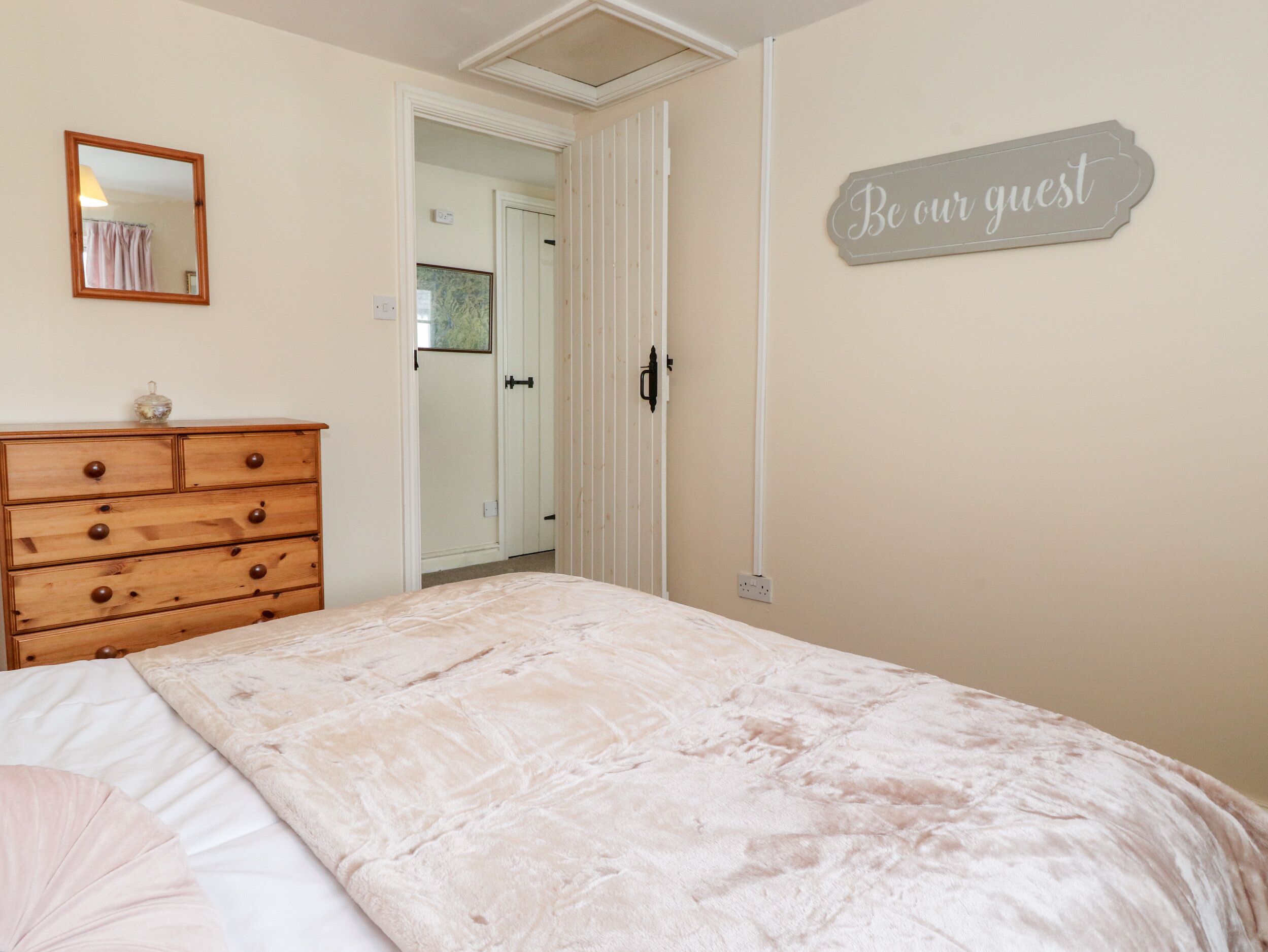 A bedroom with a bed, a dresser, a mirror, and a sign that reads "Be our guest".