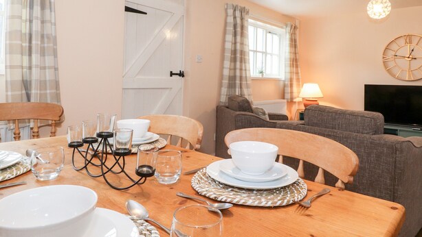 Un coin repas avec une table en bois dressée pour quatre personnes, un canapé, un téléviseur et une horloge au mur.