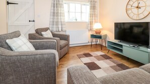 Un salon comprenant un téléviseur, deux fauteuils, un canapé, une lampe et une horloge murale.