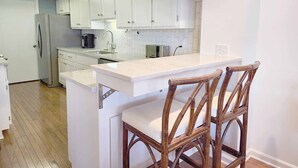 Una cocina moderna con armarios blancos, un refrigerador de acero inoxidable, una cafetera y un taburete de bar de madera.