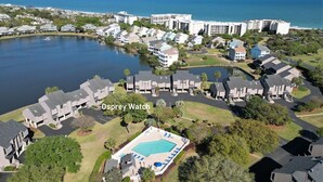 Vista aérea de Osprey Watch, que muestra una amplia piscina rodeada de edificios residenciales modernos, un lago y una vista despejada del océano.