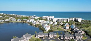An aerial view of Osprey Watch, featuring a large swimming pool surrounded by modern residential buildings, a lake, and a clear view of the ocean.