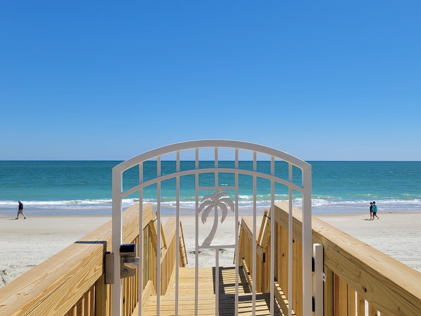 Une promenade en bois qui mène à une plage d’où l’on a une vue dégagée sur l’océan.