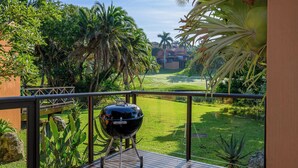 A balcony with a barbecue grill, lush greenery, and a view of a golf course. - San Lameer Villa 2705 (Southbroom)