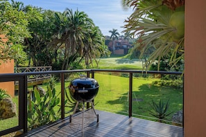 A balcony with a barbecue grill, lush greenery, and a view of a golf course. - San Lameer Villa 2705 (Southbroom)