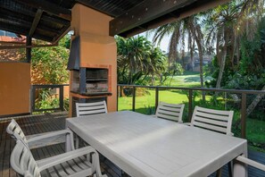 Une terrasse extérieure avec une table et des chaises, un barbecue et une vue sur un terrain de golf.