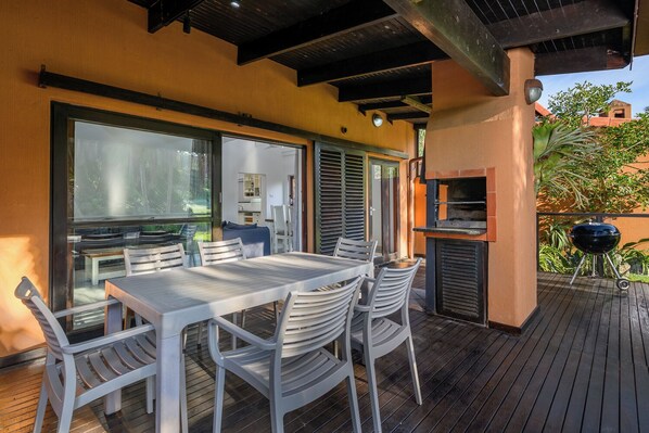 Une terrasse extérieure avec une table et des chaises, un barbecue et une vue sur un bâtiment en arrière-plan.