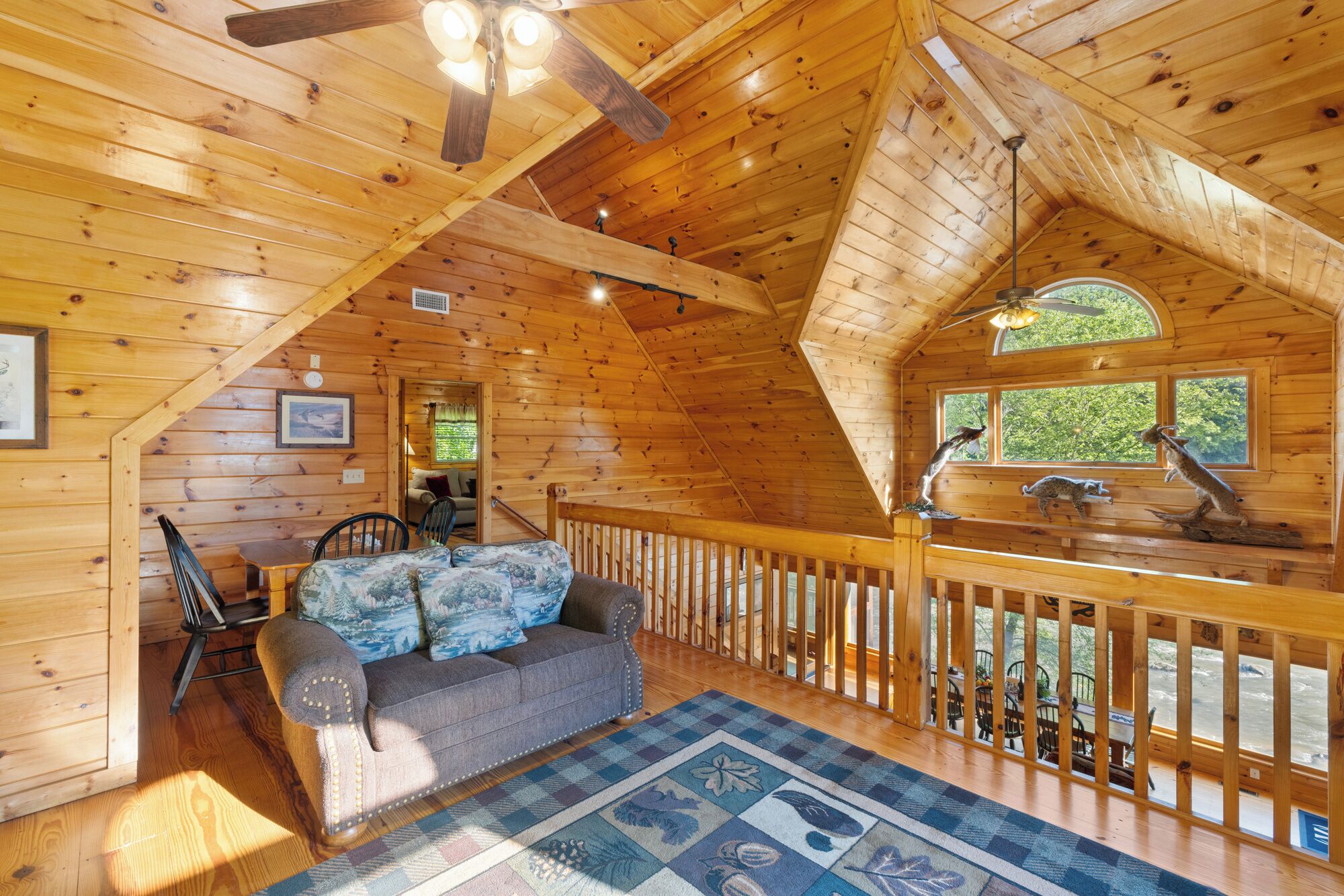 A cozy cabin with a wooden interior, a dining area with a table and chairs, a cushioned sofa, and a view through a window.