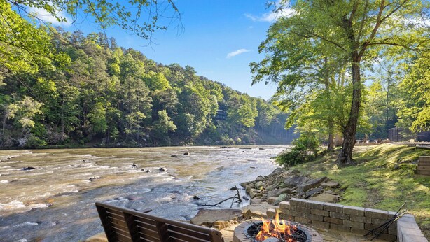 Un banco junto al río con una chimenea, rodeado de un muro de piedra y abundante vegetación.