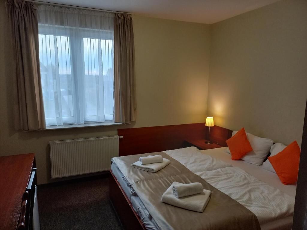 Een hotelkamer met twee bedden, een raam met gordijnen, een bedlampje en een radiator.