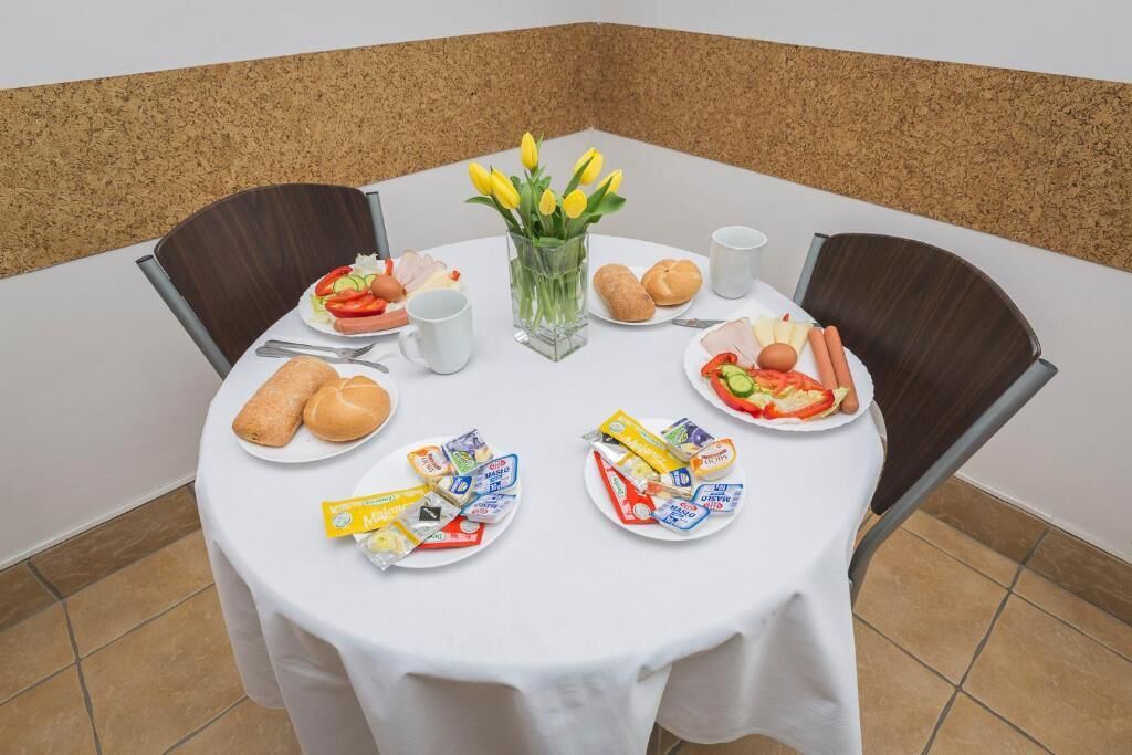 Une table ronde recouverte d’une nappe blanche, entourée de quatre chaises, mise pour un repas avec des assiettes de nourriture, du pain et des condiments.