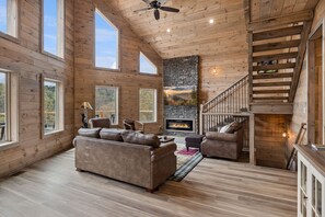 A spacious living room with a fireplace, wooden floors, and a staircase.