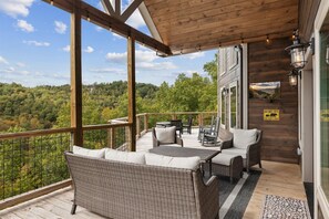 A wooden deck with wicker furniture, a table, and chairs, overlooking a forested area.