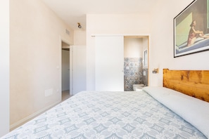 A bedroom with a bed, a wooden headboard, a shower area, and a door leading to another room.