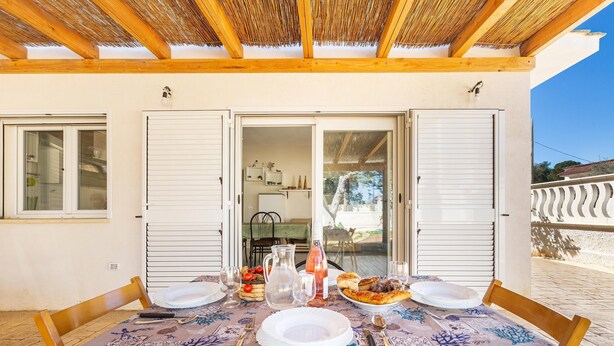 An outdoor dining area with a table set for two, a thatched roof, and a view of the interior through open shutters. - 3233 Villa Lucechiara by Barbarhouse (Avetrana)