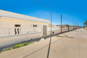 A long, straight road with a white fence on one side and a building with a beige facade on the other.
