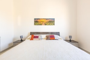 A neatly made bed with a white duvet, two pillows with patterned and solid designs, and two bedside lamps on matching nightstands.