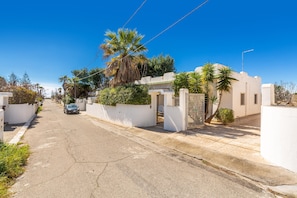 A residential street with houses, a parked car, and palm trees.