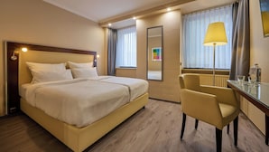 Una habitación de hotel con una cama, una silla, un escritorio con lámpara y un espejo.