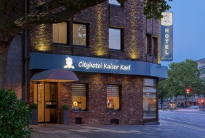 The exterior of Cityhotel Kaiser Karl, featuring a brick facade, large windows, and a prominent illuminated sign.