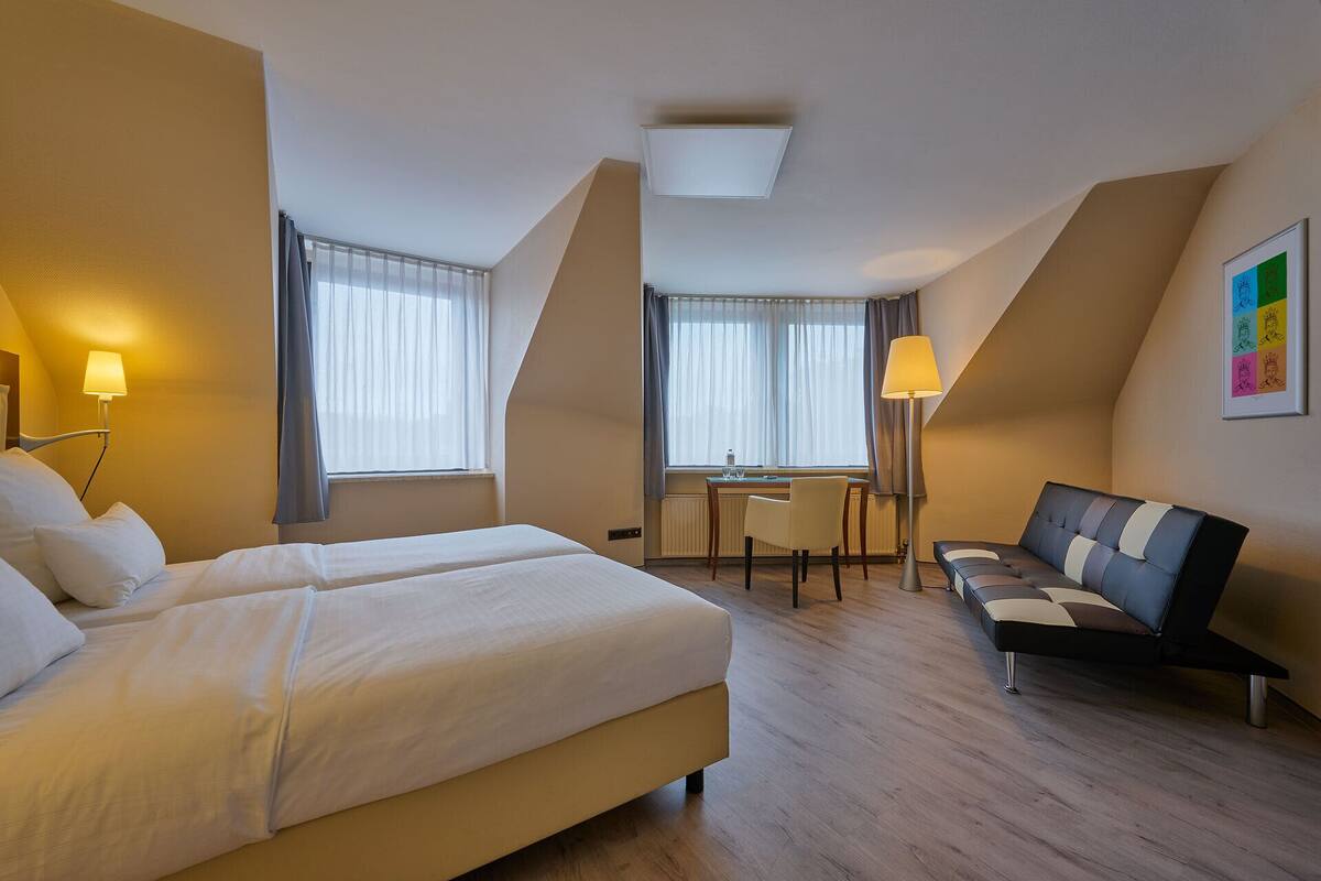 Une chambre d’hôtel avec un lit, un bureau, une chaise, un canapé et une lampe.
