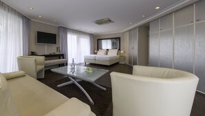 Una habitación de hotel moderna con un sofá, una mesa de centro de vidrio con manzanas, una cama, un televisor y un armario.