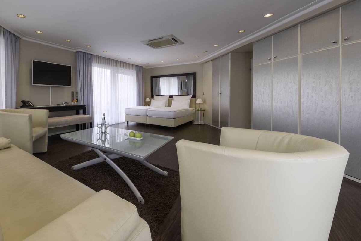 Une chambre d’hôtel moderne avec un canapé, une table basse en verre sur laquelle sont posées des pommes, un lit, une télévision et une armoire.