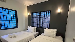 Zwei Einzelbetten mit weißen Leinen und Handtüchern, eine dunkle Wand und Fenster mit Gittermuster.