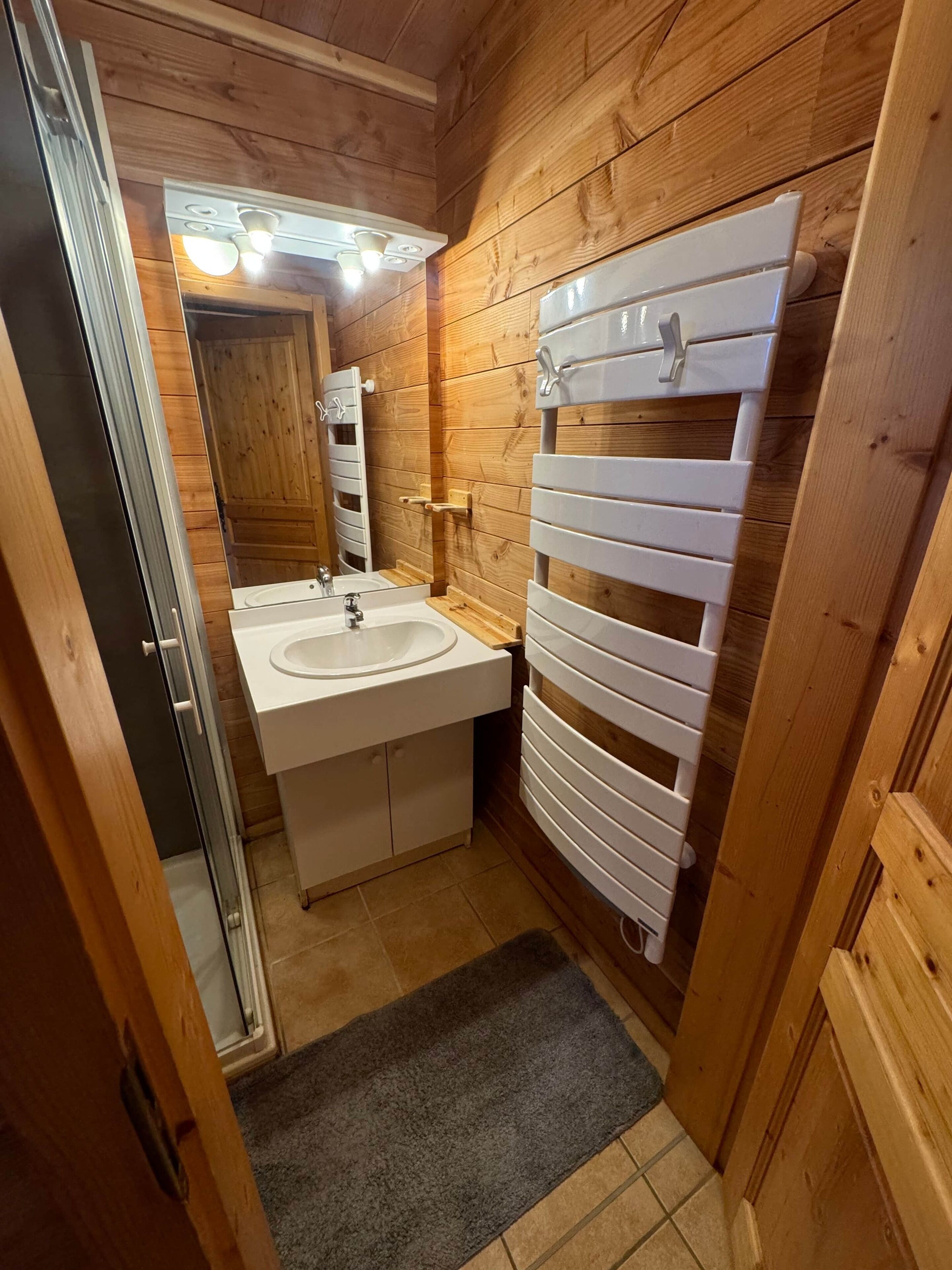 Een kleine badkamer met houten wanden, een witte wastafel en een handdoekhouder.