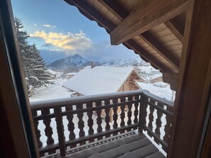 Un balcón de madera con barandilla que da a un pueblo montañoso cubierto de nieve.