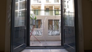 On aperçoit, à travers une porte vitrée, un balcon avec une rambarde en métal, un pot de fleurs et une chaise rouge.