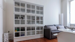 A modern living room with a grey sofa, a dining table, and a white built-in shelving unit with glass doors. - Italianway Easy - Vincenzo Monti 32 (Milan)
