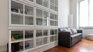 A modern living room with a grey sofa and a glass-fronted shelving unit containing kitchenware. - Italianway Easy - Vincenzo Monti 32 (Milan)