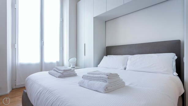 A modern bedroom with a large bed, white linens, and a grey headboard. - Italianway Easy - Vincenzo Monti 32 (Milan)
