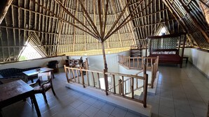 Una habitación con techo alto de paja y una escalera de madera. Hay una cama y una mesa con sillas.