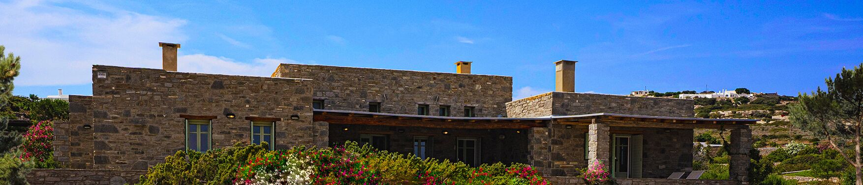 A stone building with a flat roof, multiple chimneys, and a covered porch.